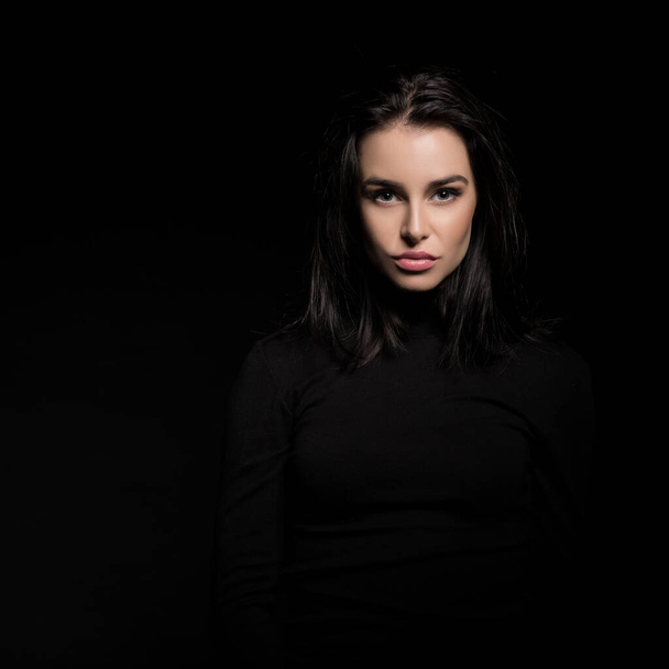 Beautiful girl with dark hair posing over black background. Young pretty woman in studio. - Фото, зображення