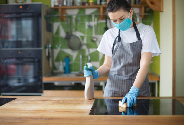 Mujer con máscara y guantes limpiando horno eléctrico con esponja
 - Foto, Imagen