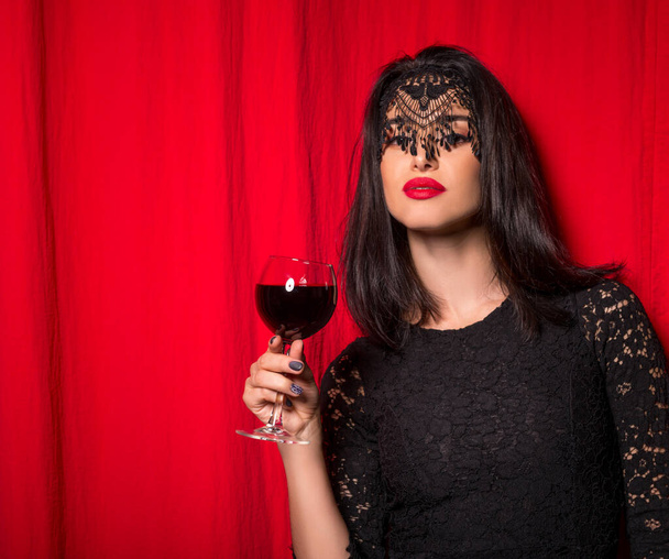Young beautiful woman holding glass of wine over red curtains - Φωτογραφία, εικόνα