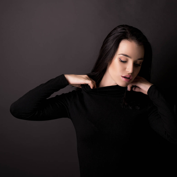 Beautiful girl with dark hair posing over black background. Young pretty woman in studio. - Photo, Image