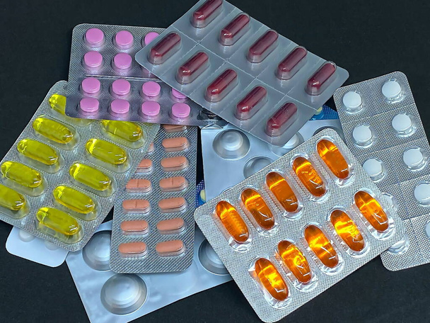 Stapel von Pillen und Vitaminen in Blisterverpackungen auf dunklem Hintergrund mit Kopierraum. Medizinisches Apothekenkonzept. Selektiver Fokus - Foto, Bild