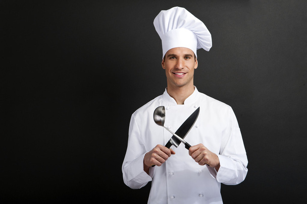 Cocinero cocinero sobre fondo oscuro sonriendo con la cuchara holdinf sombrero
 - Foto, Imagen