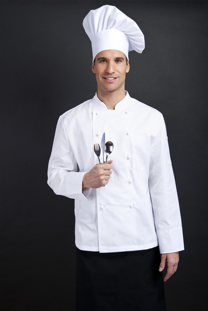 Chef cook against dark background smiling with hat holdinf spoon - Photo, Image