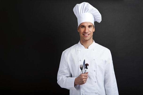 Chef cook against dark background smiling with hat holdinf spoon - Photo, image