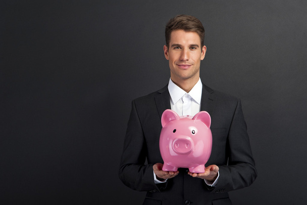 Businessman holding piggy bank against dark background - Foto, Bild