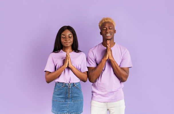 Calm black couple putting hands together in namaste or prayer gesture on lilac background - Zdjęcie, obraz