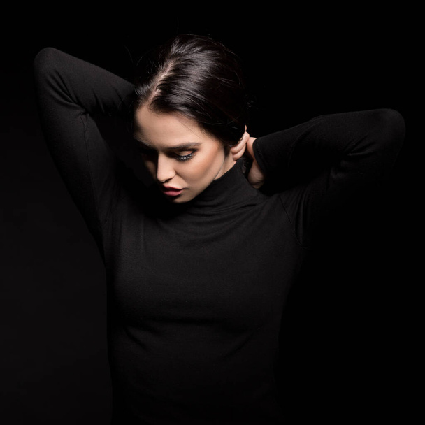 Beautiful girl with dark hair posing over black background. Young pretty woman in studio. - Фото, изображение