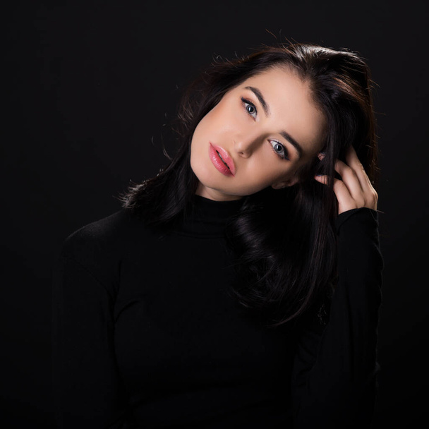 Beautiful girl with dark hair posing over black background. Young pretty woman in studio. - Foto, imagen