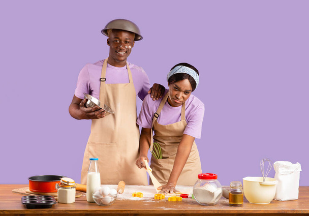 Щасливий хлопець і виснажена дівчина, покрита борошном з голови до пальця під час приготування їжі на фіолетовому фоні
 - Фото, зображення
