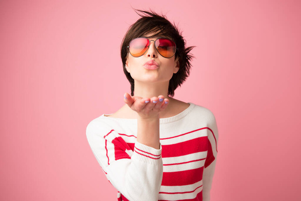 Young pretty woman looking at camera with love gesture kiss. Happy young woman in sun glasses ready to give kiss over pink background - Fotó, kép