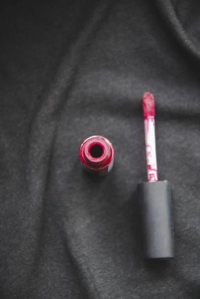 Close up imagem de batom cereja vermelha no fundo ondulado preto como brilho de lábio conceito de moda e uma escova para aplicar maquiagem. Cosméticos para estilo de moda feminina com espaço de cópia para o glamour feminino de texto
 - Foto, Imagem