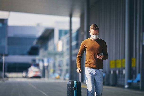Hombre con máscara facial y caminando a la terminal del aeropuerto. Temas que viajan durante pandemia y protección personal
. - Foto, Imagen