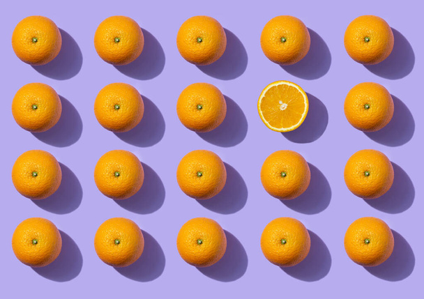 Pattern of oranges on a purple background. Fresh bright fruits. Healthy eating concept. One of the oranges is cut. - Фото, зображення