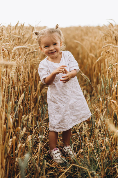 pretty cute baby girl with a beautiful smile wearing summer straw hat in a walk in the  wheat fields. selective focus. family, people concept - Foto, afbeelding