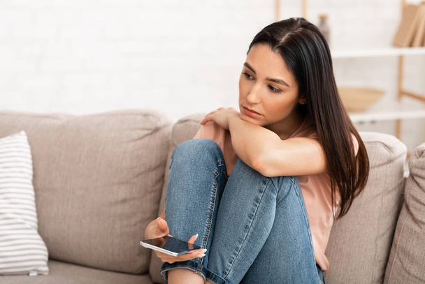 Frustrated woman holding mobile phone sitting on the couch - Photo, Image