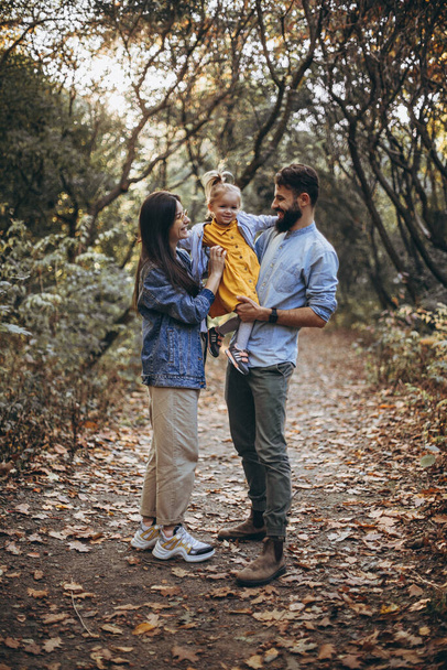 秋の公園を歩いている若いスタイリッシュなヒップスターの幸せな家族と彼らの甘い娘は晴れた天候を楽しんで - 写真・画像