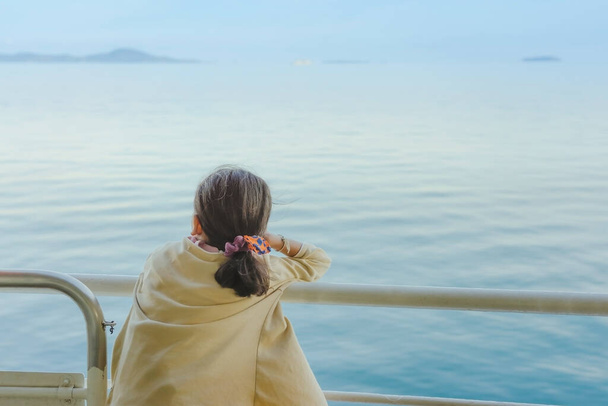 Азійська дівчинка стоїть на балюжі порому, щоб розслабитися і подивитися на океан і острів. - Фото, зображення