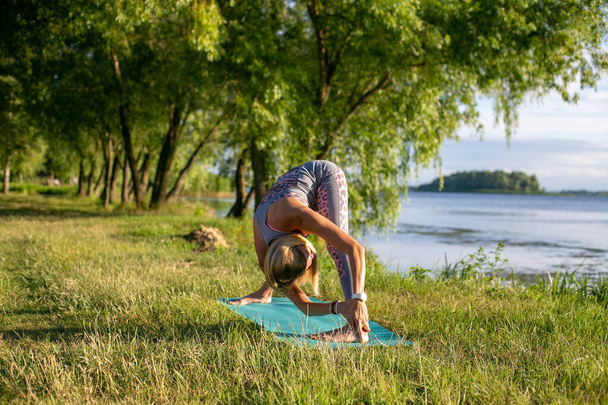 струнка жінка з довгим світлим волоссям робить йогу на відкритому повітрі на річці
 - Фото, зображення