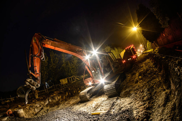 Excavadora naranja trabajando de noche en la calle
 - Foto, Imagen