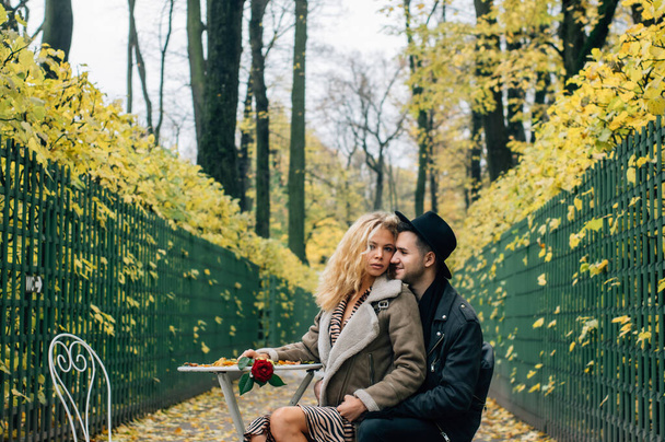 Пара сидя на стуле в центре прохода и обнимаясь, девушка держит красную розу в руке и смотрит в камеру
 - Фото, изображение