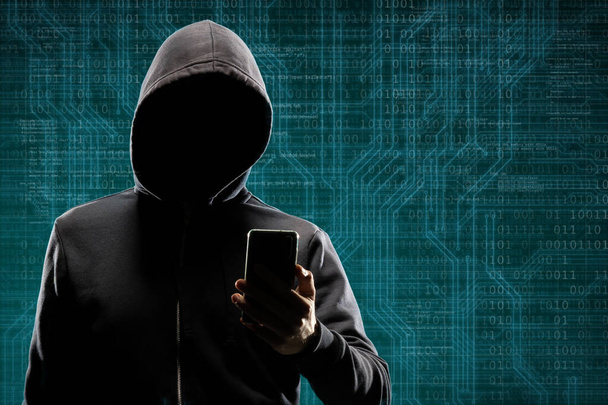 Computer hacker in mask and hoodie over abstract binary background. Obscured dark face. Data thief, internet fraud, darknet and cyber security concept. - Foto, Bild