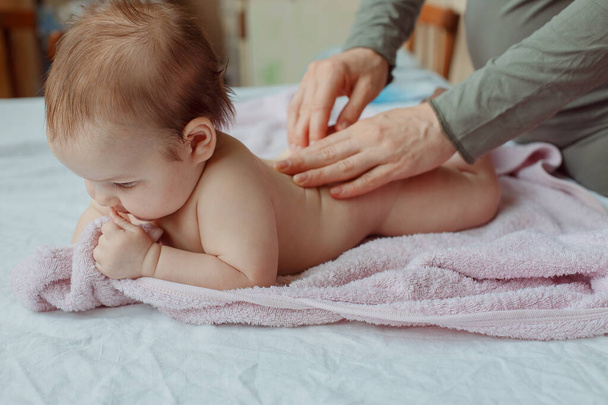 Anya keze krémet tesz a babára fürdés után a szobában. egy anya kezei, ahogy masszírozza a baba lábát, otthon az ágyban. - Fotó, kép