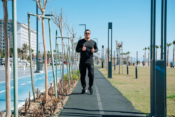 Młody mężczyzna w sportowej odzieży jogging w parku obok promenady - Zdjęcie, obraz