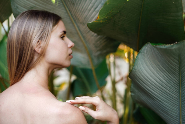 Tratamento de spa e conceito de cosméticos orgânicos. Visão perfil lateral da mulher adulta jovem com ombros nus e pele saudável em pé na natureza tropical com folhas da selva no fundo
 - Foto, Imagem