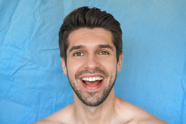 Πορτρέτο ενός νεαρού ελκυστικού άνδρα με πλατύ όμορφο χαμόγελο, τέλειο δέρμα και χτένισμα με χαρούμενη χαρούμενη έκφραση στο πρόσωπό του - Φωτογραφία, εικόνα