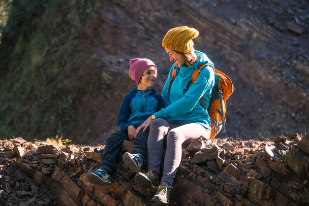 Une femme voyage avec un enfant. Mère avec un fils est assise sur un grand rocher. Montez au sommet de la montagne avec les enfants. Le garçon avec le sac à dos est monté au sommet. Vacances actives. - Photo, image