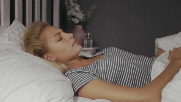 Young woman lying in the bed at night. Beautiful blond sleeping girl. Woman has a bad dream - Imágenes, Vídeo