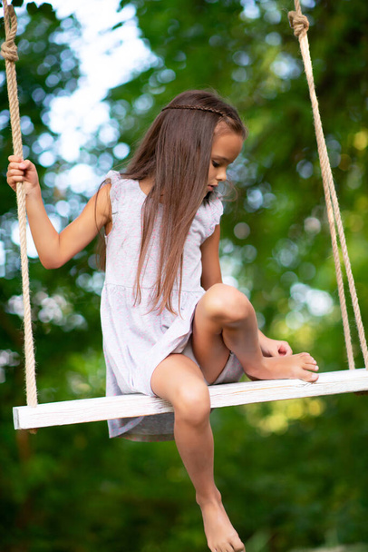 Happy girl rides on a swing in park. Little Princess has fun outdoor, summer nature outdoor. Childhood, child lifestyle, enjoyment, happiness. - Fotografie, Obrázek