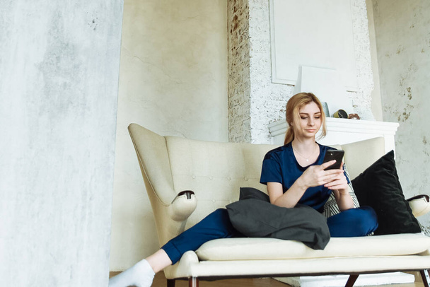 Atrakcyjna kobieta korzystająca ze smartfona siedząc na kanapie w domu. Zakupy i portale społecznościowe przez telefon. - Zdjęcie, obraz