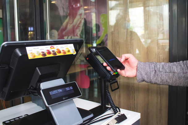 Lviv, Ukraine - May 17, 2020 : McDonalds restaurant, customer is paying with smartphone using NFC technology contactlessly. Contactless and social distance concept, reopening business - 写真・画像