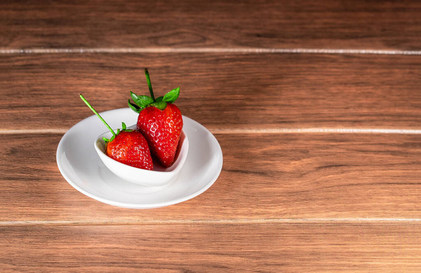 fresas rojas frescas con tallo verde en platos de cerámica blanca dejados en una mesa de madera
 - Foto, Imagen