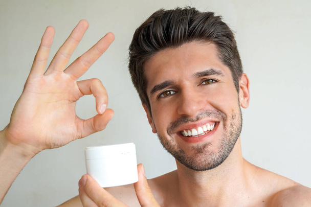 Giovane bell'uomo con una pelle e capelli perfetti sta mostrando un prodotto nel suo bagno con un ampio sorriso
 - Foto, immagini