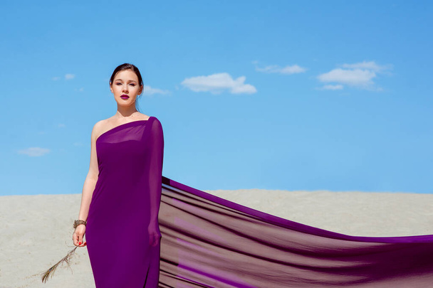 Úžasná krásná brunetka s peřím v purpurové látce v poušti. Oriental, indický, módní, styl koncepce - Fotografie, Obrázek