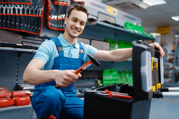 Trabalhador masculino feliz em uniforme escolhendo caixa de ferramentas na loja de ferramentas. Escolha de equipamentos profissionais na loja de ferragens, supermercado de instrumentos
 - Foto, Imagem