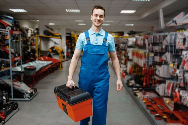 Trabajador masculino sonriente en uniforme que compra la caja de herramientas en la tienda de herramientas. Elección de equipos profesionales en ferretería, supermercado de instrumentos
 - Foto, imagen