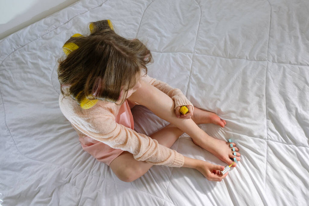 the girl on the bed paints her toenails in yellow - Фото, зображення