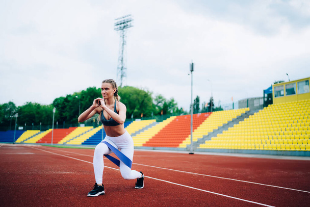 Focused active lady full of motivation diligently training on stadium and lunging with ribbon while looking away during hard workout - Φωτογραφία, εικόνα
