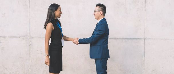 Side view of diverse young man and woman standing on street and shaking hands meeting on business conference and greeting each other - Photo, Image