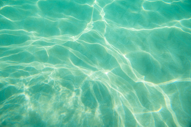 Onder water. Zonneschijn onderaan de stoel. Golven onder water en zonnestralen die doorschijnen. Diep turkoois blauwe zee. Oceaan. Transparant water en licht op zand. - Foto, afbeelding