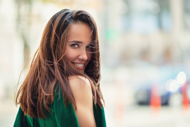 Young pretty likable cheerful woman posing summer city outdoor. Beautiful self-confident girl dressed in emerald-colored jumpsuit with long brown hair walking street enjoing her life, urban lifestyle - Fotografie, Obrázek