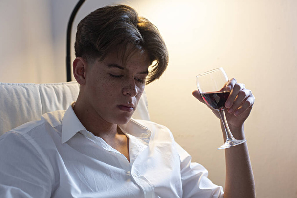 Retrato de un joven con camisa blanca bebiendo vino en casa
. - Foto, Imagen