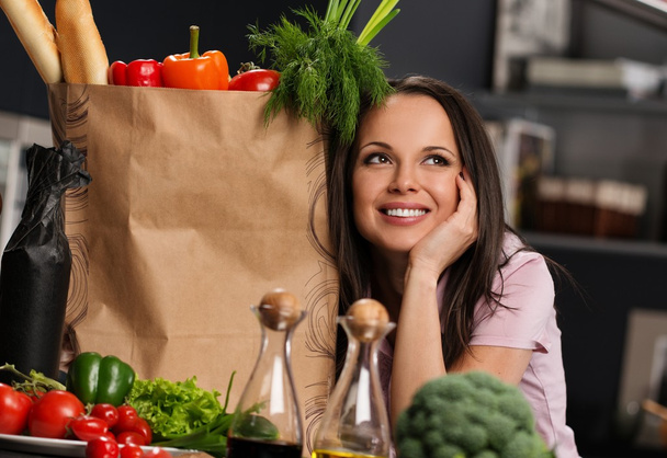 Mujer joven con bolsa de supermercado llena de verduras frescas en una cocina moderna
 - Foto, imagen