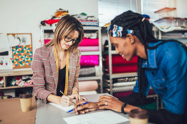 Δύο νεαρές επιχειρηματίες γυναίκες, ή σχεδιαστές μόδας που εργάζονται στο ατελιέ - Φωτογραφία, εικόνα