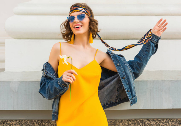 stylish attractive woman in hippie style outfit, yellow dress denim jacket, trendy accessories, sunglasses, smiling, happy positive mood, street fashion, spring summer fashion trend, cheerful emotion - Photo, image