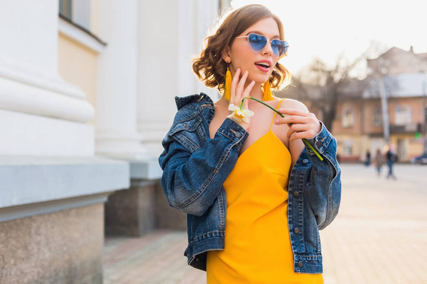 bright portrait of beautiful woman holding flower, yellow dress, denim jacket, hipster style, summer fashion trend, smile, trendy sunglasses - Valokuva, kuva