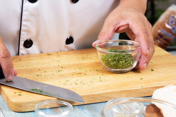 Chef κρατήσει φλιτζάνι ψιλοκομμένο μαϊντανό για το μαγείρεμα σκορδόψωμο / Μαγειρεύοντας Σκόρδο έννοια ψωμί - Φωτογραφία, εικόνα